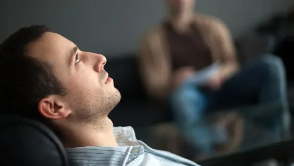 Man reclining in a chair during a therapy session, looking upward while a blurred therapist sits in the background.