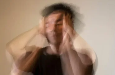 Blurred image of a person in a dark shirt with hands on the sides of their head, suggesting stress or overwhelm.