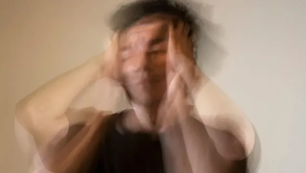 Blurred image of a person in a dark shirt with hands on the sides of their head, suggesting stress or overwhelm.