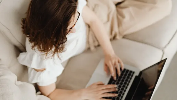 How Online Therapy Makes Mental Health Support More Accessible Person with brown hair using a laptop on a beige sofa, seen from above, wearing a light top and glasses