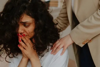 A woman with curly hair covers her mouth in distress as another person places a comforting hand on her shoulder.