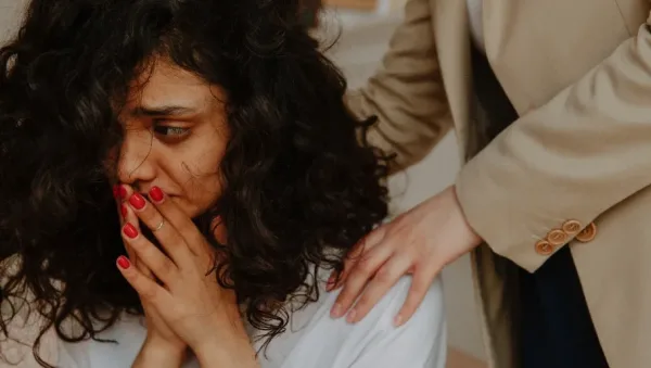 IFS Therapy for Trauma Recovery A Practical Guide A woman with curly hair covers her mouth in distress as another person places a comforting hand on her shoulder.