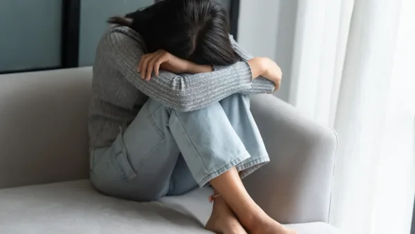 Top 10 Evidence-Based Approaches to Anxiety Therapy Person sits curled on a light gray couch, arms resting on their knees with head down, conveying distress or sadness.