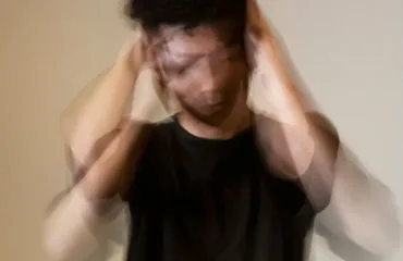 Blurred image of a person in a black shirt holding their head, suggesting stress or overwhelm due to quick movements.