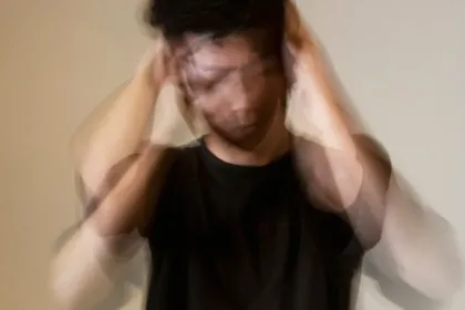 Blurred image of a person in a black shirt holding their head, suggesting stress or overwhelm due to quick movements.