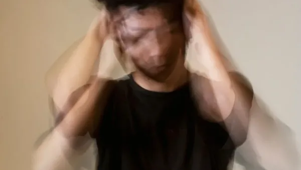 Blurred image of a person in a black shirt holding their head, suggesting stress or overwhelm due to quick movements.